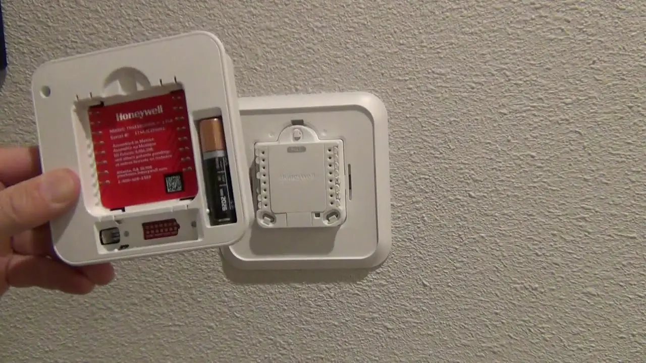 a person changing the battery of honeywell thermostat